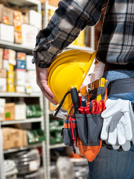 Electrician in the electrical component store holds the helmet and goggles in his hand. Construction industry, electrical system. View from behind.